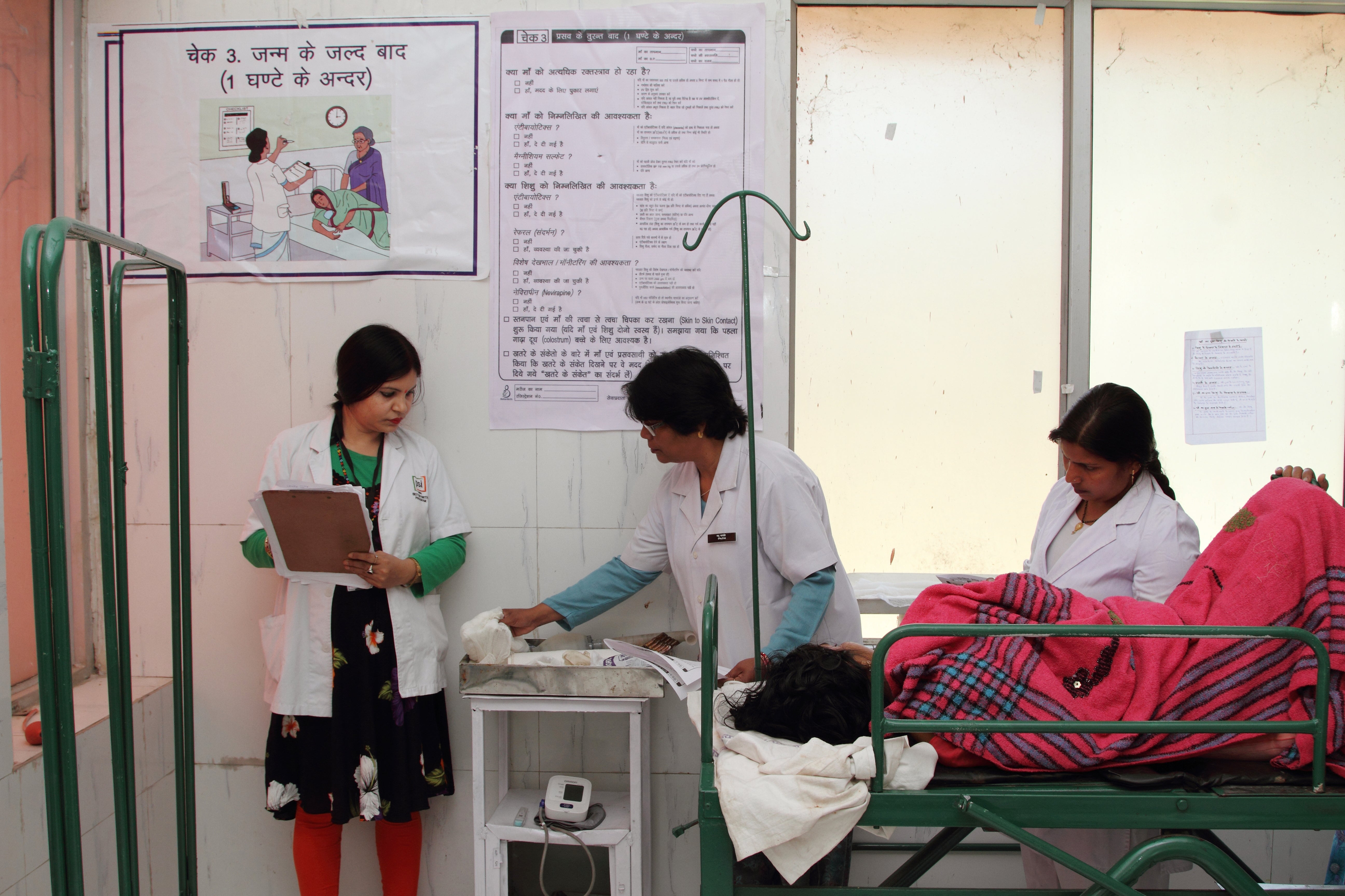 Birth attendants and a BetterBirth coach use the Safe Childbirth Checklist, hanging on the wall, at a facility in Uttar Pradesh to ensure quality care the new mother and baby.