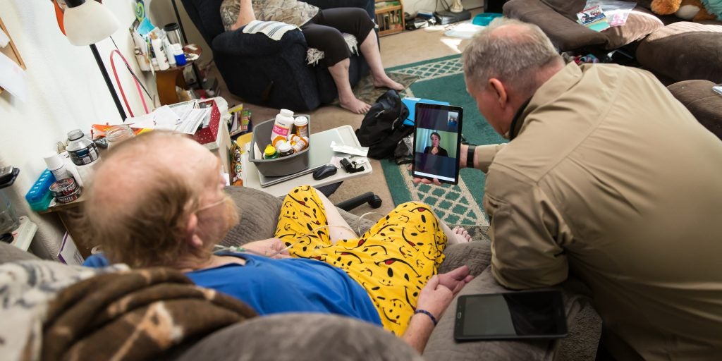 Mock patient and paramedic speak with clinician on a tablet in the patients living room in rural Utah