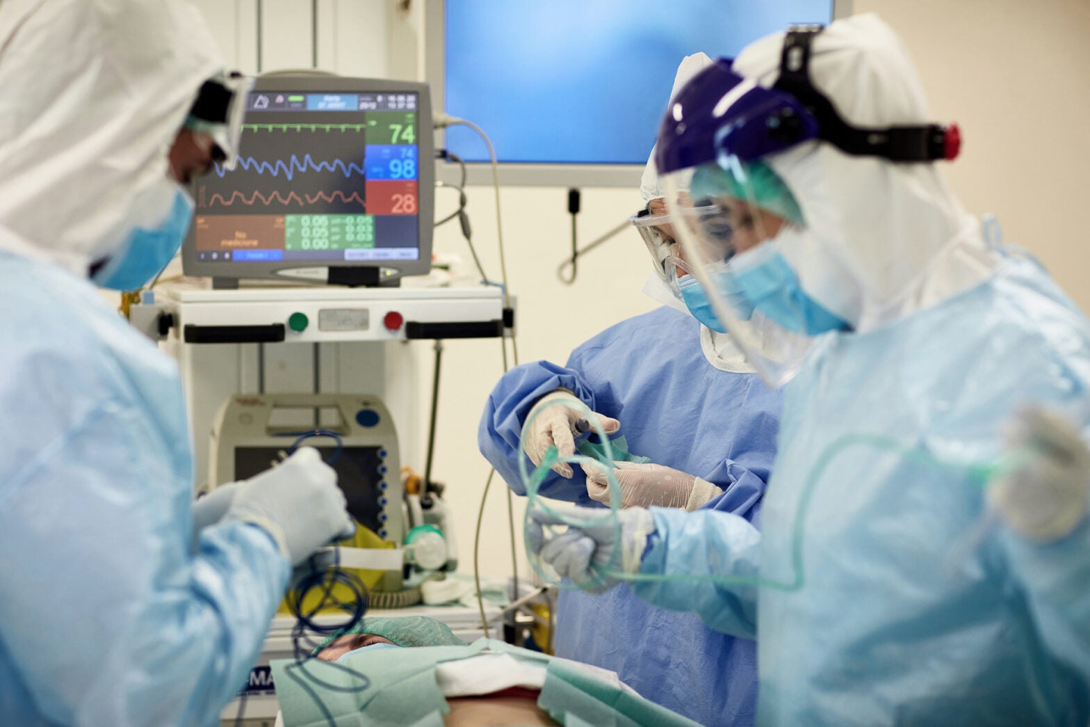 Doctors and nurses wearing surgical gowns over protective suits, eyewear, face shields, and masks as they prepare for surgical procedure.