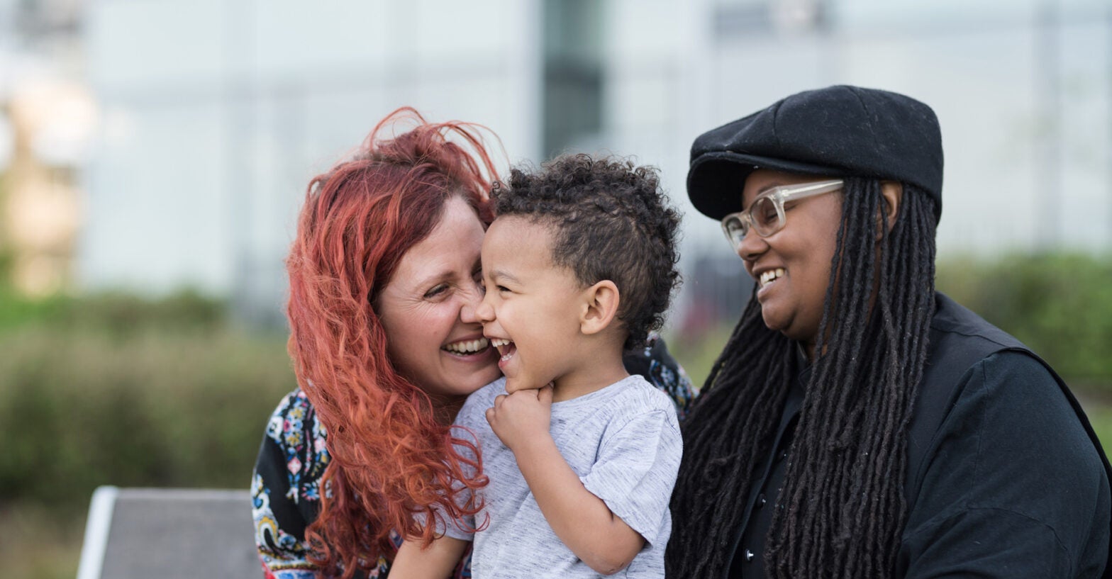 Two mothers holding their son on their laps outside at the park