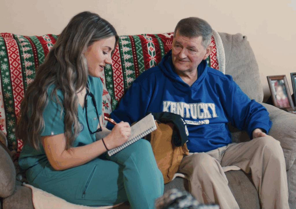 A nurse talks to a patient while sitting on a couch at the patient's home 
